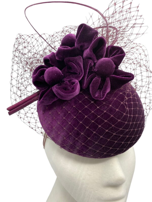 Purple velvet headpiece with veiled detail and finished with a curled quill.